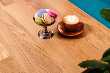 macaroons in a metal bowl and a cup of coffee on a wooden table