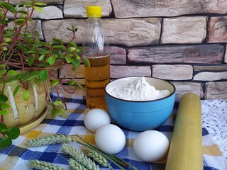 Still life of food on the kitchen table a bowl of flour chicken eggs a bottle of sunflower oil wheat ears a wooden rolling pin indoor flower