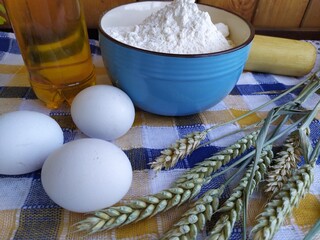 Still life of food on the kitchen table a bowl of flour chicken eggs a bottle of sunflower oil wheat ears a wooden rolling pin indoor flower