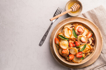 Bowl with tiny cereal pancakes with strawberries, mint and honey on a gray concrete background. Fashionable food. Mini cereal pancakes. Pancake porridge.