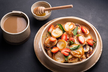 Bowl with tiny cereal pancakes with strawberries, mint and honey on a black background. Fashionable food. Mini cereal pancakes. Pancake porridge.