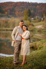 The guy and the girl are hugging on the background of the lake and autumn forest.