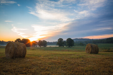 Hay bales rolled on field at sunrise with fog creates amazing sky in early summer Sussex County NJ 