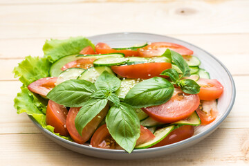 Traditional salad of slices of cucumber, tomatoes and sesame seeds on a plate on a wooden table. Vegetarian food