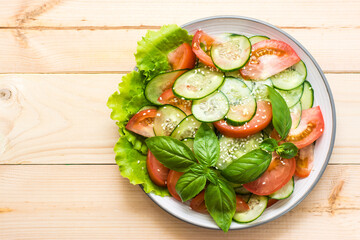 Traditional salad of slices of cucumber, tomatoes and sesame seeds on a plate on a wooden table. Vegetarian food. Top view