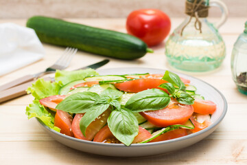 Traditional salad made of slices of cucumber, tomatoes and sesame seeds on a plate and ingredients for cooking on a wooden table. Vegetarian food