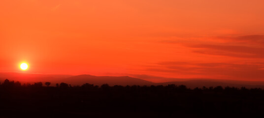Sunset landscape panoramic view, red sky and black forest silhouette. Few clouds on orange sky.