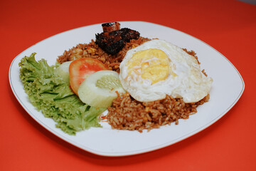 Indonesian fried rice with sunny side up and grilled spare ribs. fresh tomato lettuce and cucumber