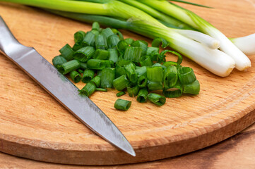 Cutted green onion with knife on the cutting board.