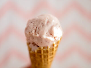 Melting baby-pink color Ice Cream on a waffle cone against pink and white zigzag pattern background.