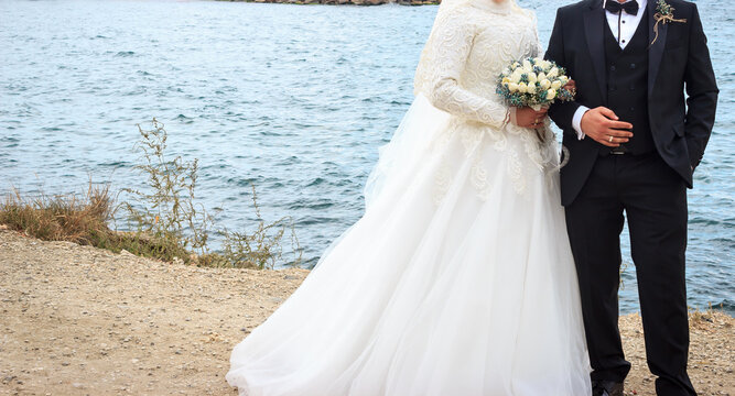 Muslim bride and groom near the sea on the beach during a wedding ceremony. Bride holds in her hand a bouquet. Groom and bride without face.