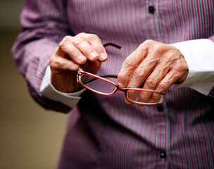 Hands of elderly woman with arthritis holding glasses