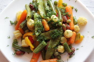 Plate of stir fry vegetables on wooden table. Top view. Summer salad in white plate.