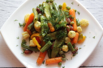 Plate of stir fry vegetables on wooden table. Top view. Summer salad in white plate.