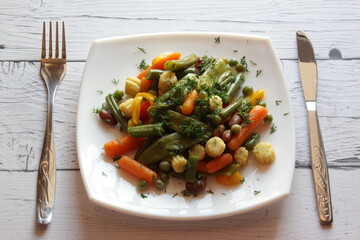 Plate of stir fry vegetables on wooden table. Top view. Summer salad in white plate.