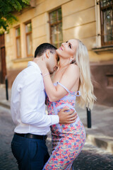 Fototapeta premium Lovely couple walking around the block. Dark-haired man in a white shirt hugging a blonde in a beautiful dress