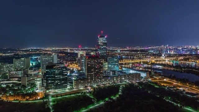 Aerial panoramic view over Vienna city with Donau City skyscrapers, historic buildings and a riverside promenade night timelapse in Austria. Illuminated skyline from Danube Tower viewpoint