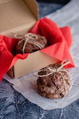 Homemade chocolate chip cookies on red paper in a craft cardboard box on a dark background. DIY gift.