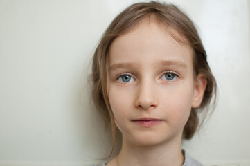 Portrait of a little girl with long blond hair and blue eyes with ponytail is standing on white background in studio