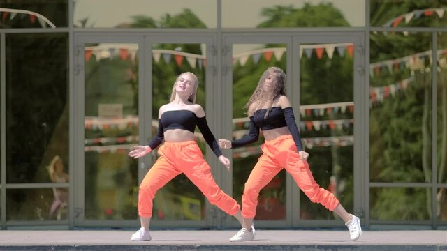two young women with long hair in tracksuit dancing dancehall twerk, street modern dance in front of the building. Booty Dance