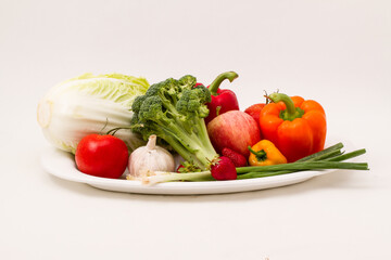 Vegetable and fruit platter isolated on a white background - lettuce, bell peppers, onions, tomatoes, broccoli, strawberries, an apple