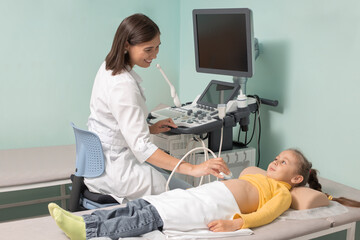 Doctor making abdominal ultrasound for child girl using scanner machine, side view. Woman runs ultrasound sensor over patient tummy looking at screen. Diagnostic examination of internal organs.