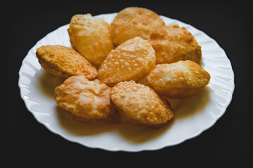 Traditional Indian deep fried poori on white plate with black background.