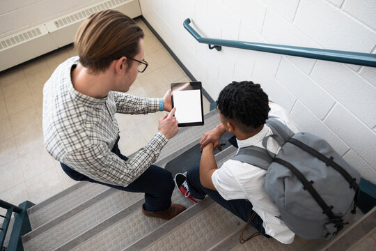 High school teacher with digital tablet talking to student on steps