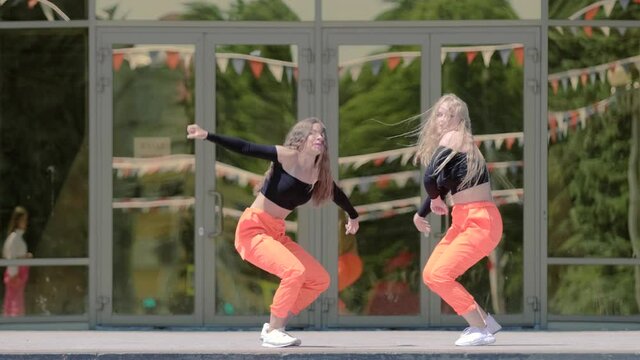 duet of two young women performing contemporary dance, dancehall twerk opposite the building with mirrored glass. Booty Dance. Slow motion