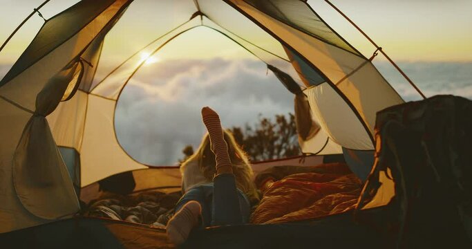 Beautiful woman camping in tent above the the clouds, watching amazing sunset, outdoor adventure lifestyle