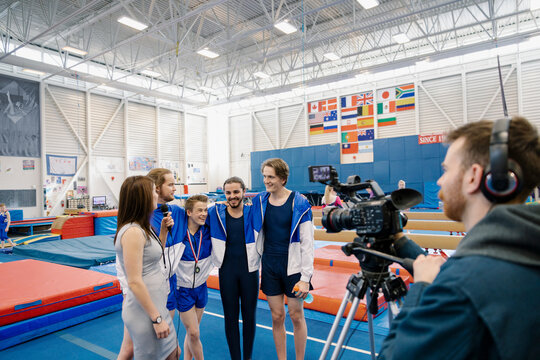 TV reporter interviewing gymnasts in gymnasium