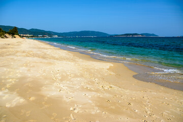 Sunny day, sand creaking, clear turquoise sea, coral reefs on the coast of Yalong Bay in South China Sea. Sanya, island Hainan, China.