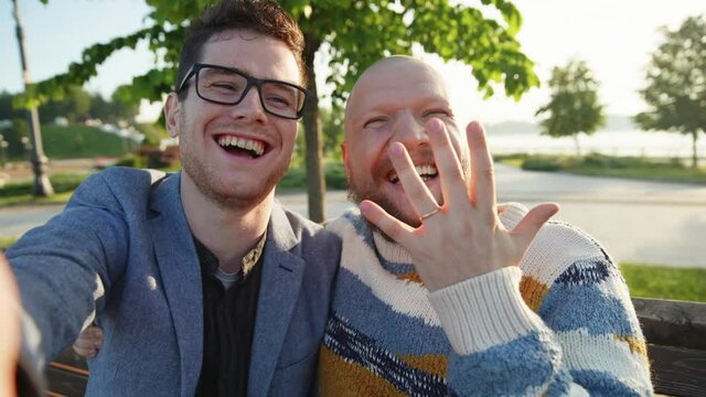 Sefie portrait of young gay couple feeling happy showing ring. LGBTQ men smile to camera. A guy make proposal of mariage to his boyfriend. LGBTQI, Pride Event, LBGT Pride Month, Gay Pride Symbol
