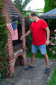 Young Man Dad Doing Food BBQ Barbeque Grill In The Garden For His Family With USA US American Flag Celebrating 4th 4 Fourth July Independence Day Traditional Way Wearing N95 Face Mask Due Coronavirus