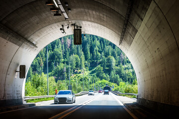 Road tunnel in Alpine mountains, Switzerland. Inside the modern tunnel and view of entrance to next tunnel in summer.