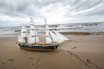 Antiquarian wooden scale model of the clipper tall ship, close-up. Dramatic sky and sea shore in...