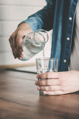 The man pours himself a glass of clean water. A carafe of water on the kitchen wooden table. Bottle...