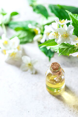 Aromatic oil in glass bottle with fresh jasmine flowers on a light gray concrete background. Flower essential oil, osmetic oil perfume .