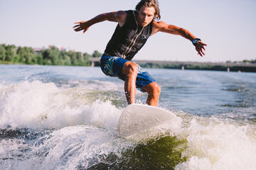 A man is surfing on a surfboard drawn by a motor boat above the wave of the boat. Weixerfer is...