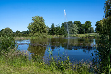 Fountain in a pond in a natural park against a blue sky, beautiful rural landscape in summer