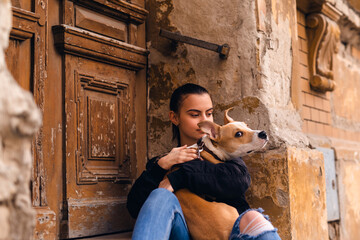 A young caucasian teenage  girl is sitting on the steps of an old abandoned house with her dog...