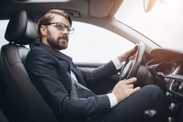 Successful bearded businessman in eyeglasses and formal clothing driving modern car with seatbelt. Concept of male career, vehicle and safety.