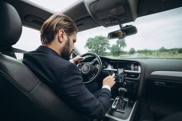 Handsome bearded businessman in formal clothing driving car and using gps navigation on smartphone. Concept of people, technology and transportation.