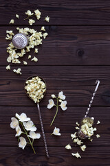 Fototapeta na wymiar Dried jasmine flowers for tea and retro tea strainers on a dark wooden background. Composition of fresh and dried jasmine flowers with copy space for text. Making aromatic tea. Top view.