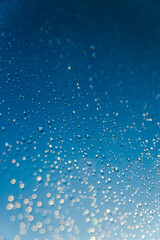 Naklejka na ściany i meble Blurred water drops on sky background, bokeh on blue background.