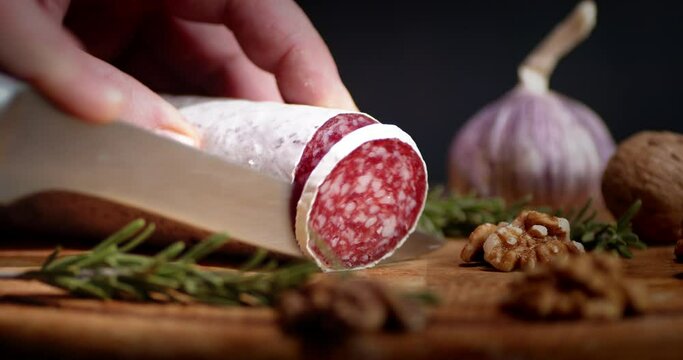 The hand of a man with knife to cut salami on a cutting Board.