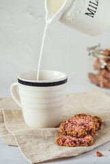 Crispy, gluten free oat cookies with blackberry and nuts. Freshly baked, healthy dessert with fruits pulp leftovers and healthy nuts. Cookies on the cloth with cup and milk.  Closeup.
