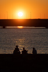 Naklejka na ściany i meble Silhouettes of people enjoying seascapes on the shore during sunset.