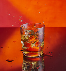 Cool whisky splash shot,taken on reflective surface with red/orange gradient background.