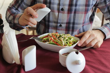 Photo for the restaurant menu. A young guy in a checkered shirt eats chicken salad with mayonnaise.